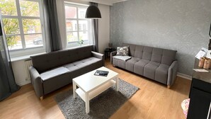 A modern living room with two grey sofas, a white coffee table, and a large window with curtains.