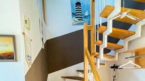 A wooden staircase with cat trees on each landing, a painting of a lighthouse, and a broom on the floor. - für 4 Personen ca. 64 m² in Ahlbeck, Norddeutschland (Mecklenburg-Vorpomme by Interhome (Ahlbeck)