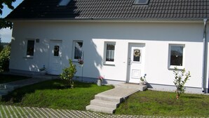 A white two-story house with a tiled roof, a front porch, and a small front yard with a pathway leading to the door. - für 4 Personen ca. 64 m² in Ahlbeck, Norddeutschland (Mecklenburg-Vorpomme by Interhome (Ahlbeck)
