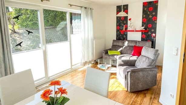 A modern living room with a white dining table, grey sofa, and a large window with curtains. - für 4 Personen ca. 64 m² in Ahlbeck, Norddeutschland (Mecklenburg-Vorpomme by Interhome (Ahlbeck)