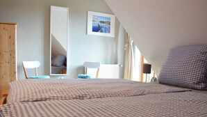 A bedroom with a checkered bedspread, a chair, a desk, and a framed picture on the wall.