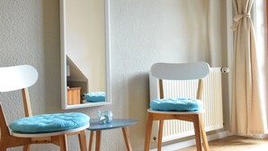 A room with two wooden chairs with blue cushions, a small round table, a white radiator, and a framed picture on the wall.