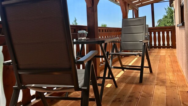 A covered outdoor seating area with wooden flooring and metal chairs.