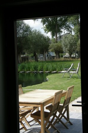 Eine Terrasse mit Tisch und Stühlen, ein Teich und Bäume.