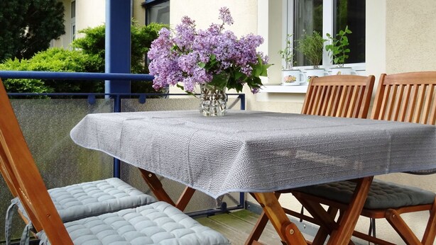 A wooden deck with a table covered by a textured tablecloth, surrounded by cushioned chairs. - - Alte Kelterei by Interhome (Dresden)