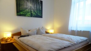 A double bed with a wooden frame, two bedside tables with lamps, a forest-themed wall art, and a window with sheer curtains. - - Alte Kelterei by Interhome (Dresden)