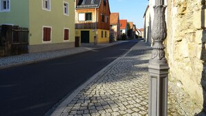 A cobblestone street lined with historic buildings, including a yellow house with a wooden balcony and a stone wall with a decorative column. - - Alte Kelterei by Interhome (Dresden)