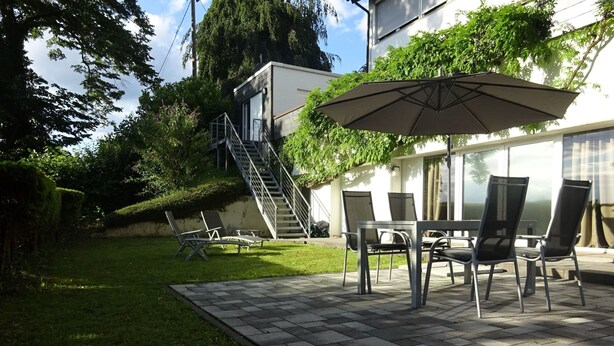 Ein Patio mit Tisch und Stühlen, einem beschatteten Sonnenschirm und einer Treppe, die zu einer erhöhten Ebene führt.