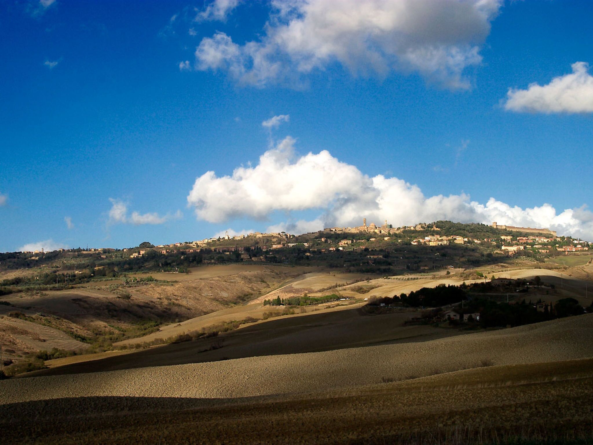 Paisaje rural con colinas ondulantes, cielo azul despejado y nubes dispersas.