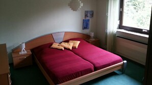 Habitación de hotel con cama, dos mesitas de noche, aire acondicionado instalado en la pared, ventana con cortinas y un cuadro en la pared.
