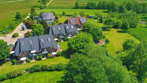 Et boligområde med flere huse, en stor grøn mark og en sø i baggrunden.
