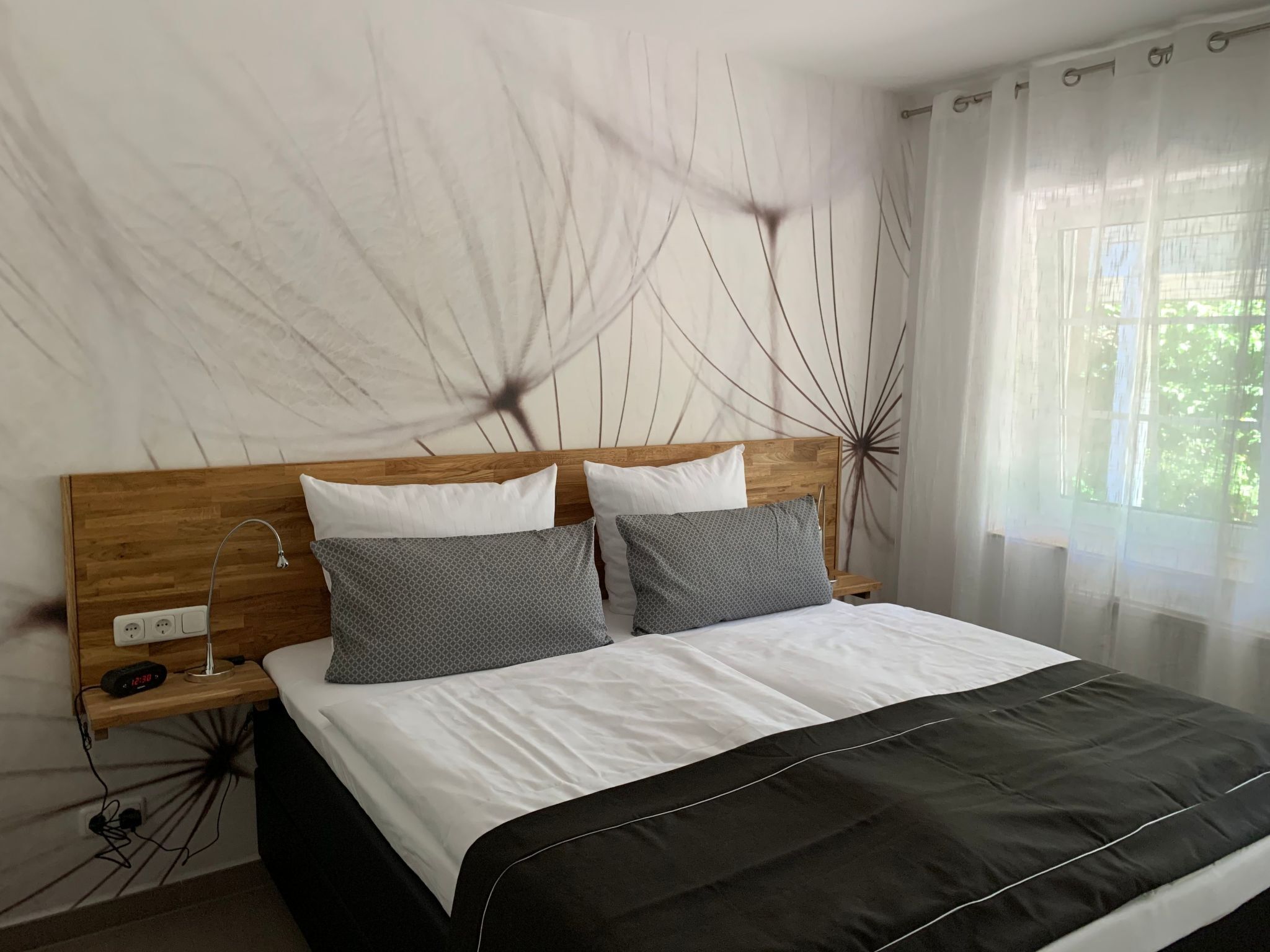A bedroom with a wooden headboard, two bedside tables, a bed with white and black bedding, and a wall with a decorative pattern.