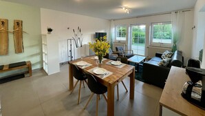En moderne stue med spiseområde, med et træbord, sorte stole, en sofa og en kaffemaskine.