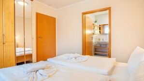 Hotellihuone, jossa on kaksi sänkyä, puinen vaatekaappi ja kylpyhuone, joka näkyy avoimesta ovesta.
