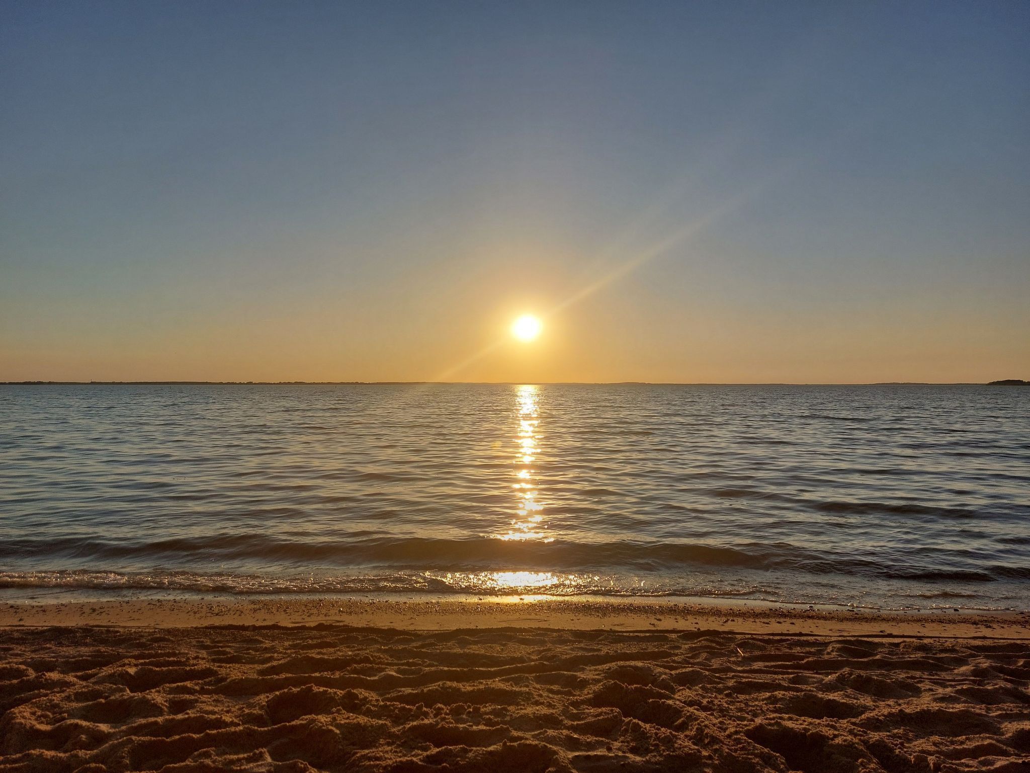 A beach with the sun setting over the water.