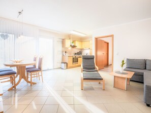 Ein modernes Wohnzimmer mit einer Couch, einem Esstisch mit Stühlen, einer Küchenzeile und einer Tür zu einem anderen Raum.