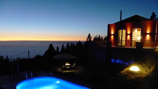 Ett modernt hus med en swimmingpool i skymningen, med utsikt över en sjö eller ett hav.