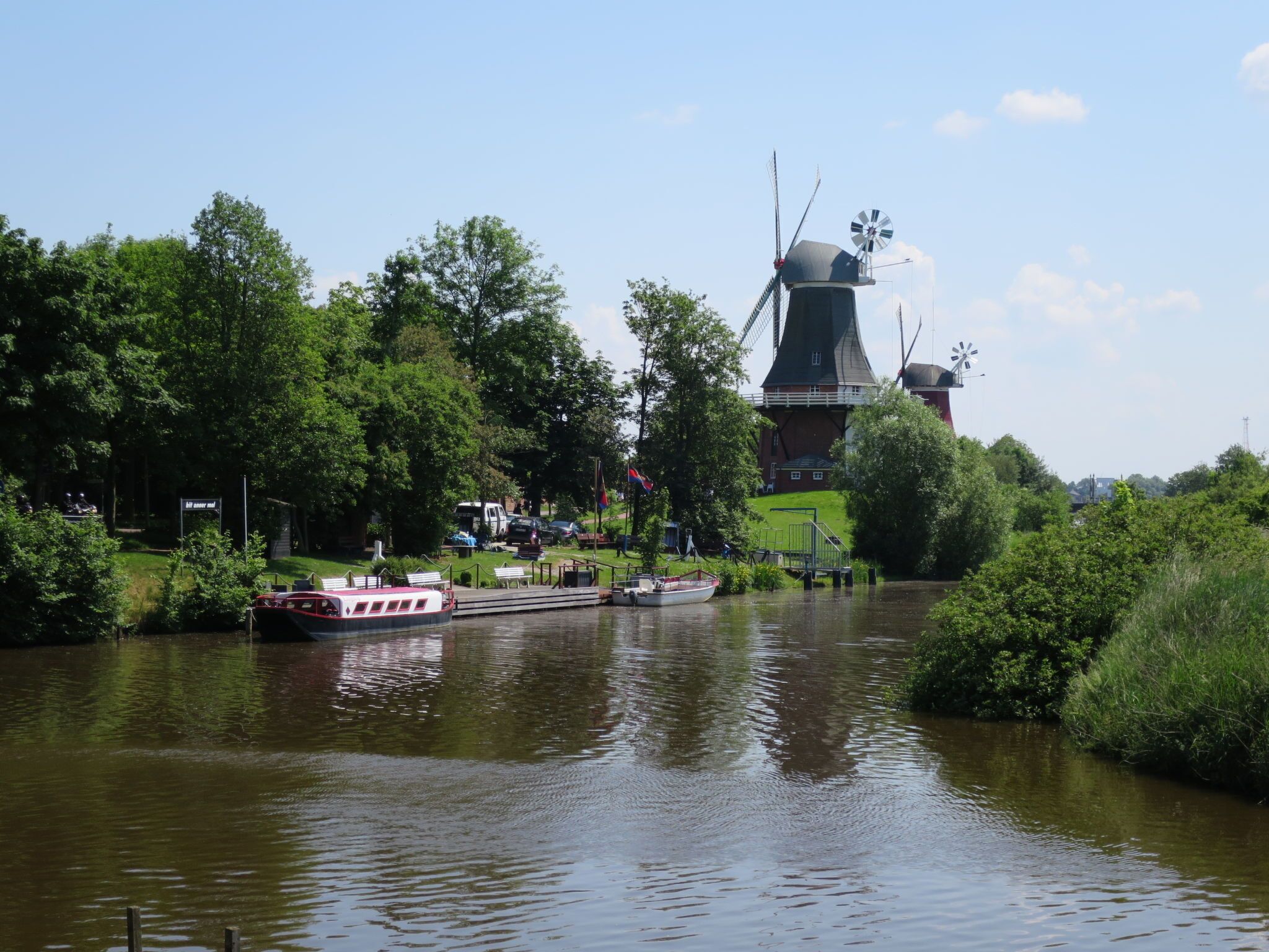 A river with boats, a windmill, and lush greenery.