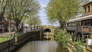 Un canal con un puente de ladrillo, árboles y un edificio con una terraza de madera.