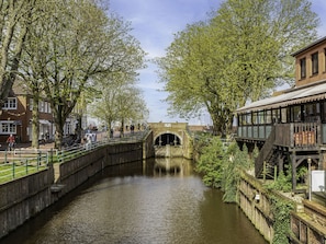Ein Kanal mit einer Ziegelbrücke, Bäumen und einem Gebäude mit einer Holzterrasse.