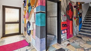 Une pièce avec un mur aux motifs colorés, un sol carrelé, une moquette rouge et un escalier.