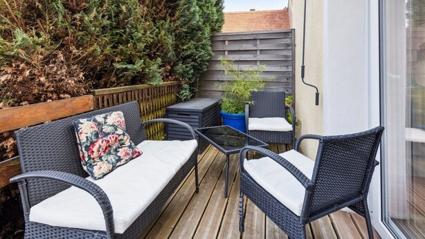 Une terrasse avec des meubles en osier, une plateforme en bois et une grande haie.