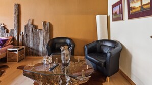 Un salon comprenant une table basse en verre, deux fauteuils en cuir noir, un buffet en bois et un grand morceau de bois flotté.