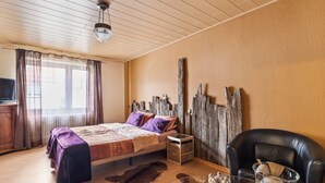 Une pièce comprenant un lit, une chaise, un téléviseur, un plafond en bois et une fenêtre avec des rideaux.