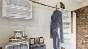 Une salle de bain rustique avec un plancher en bois, des étagères blanches, un peignoir suspendu, un pichet en céramique et un miroir.