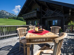 A wooden deck with a table set for dining, surrounded by chairs, and a view of a mountain in the background. - Erhöhte und ruhige Lage am Ortsrand von Bad Aussee by Interhome (Bad Aussee)