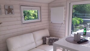 Um sofá de couro branco, uma mesinha com um controle remoto e uma janela com vista para o verde.