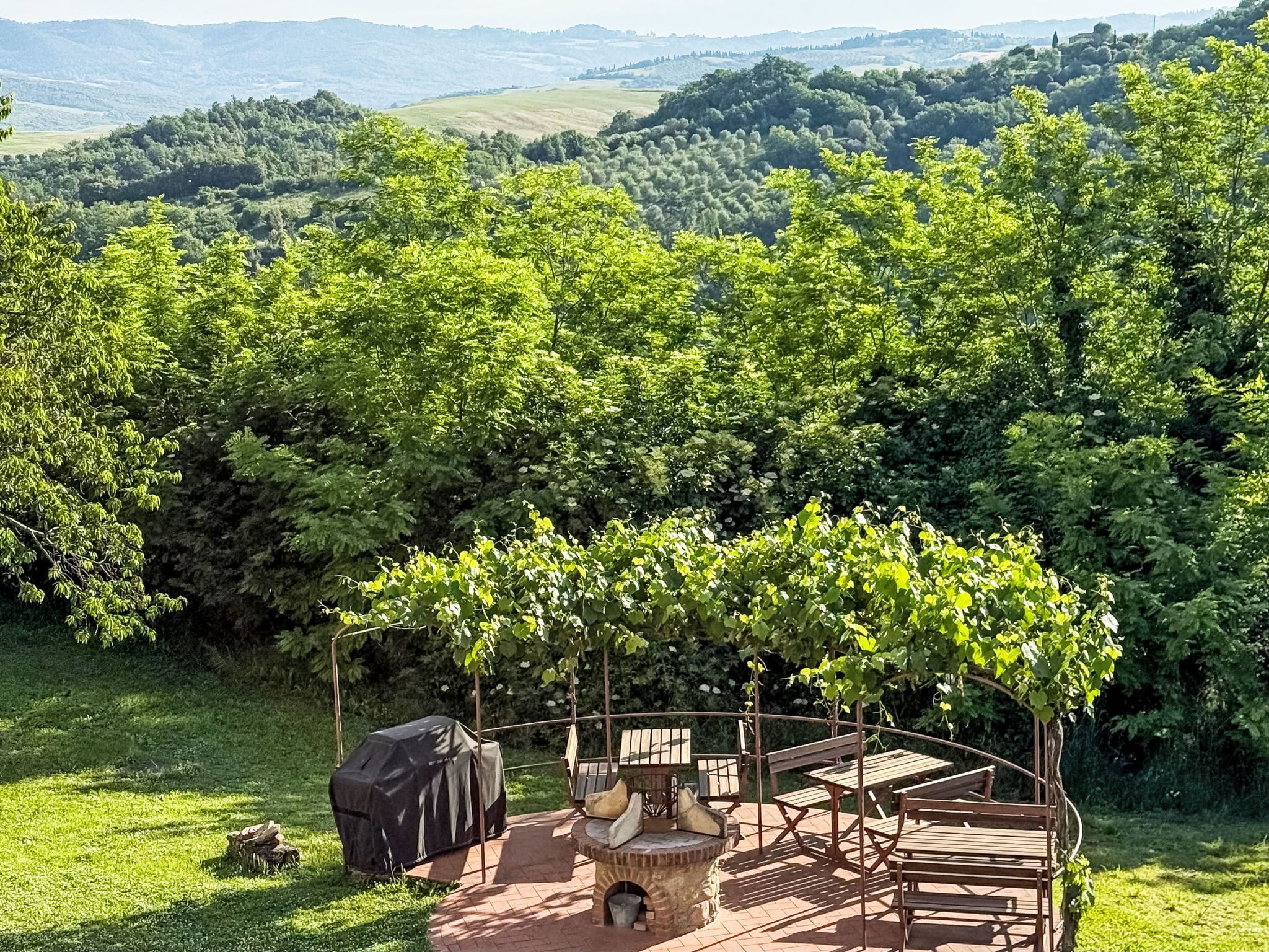 Um pátio com churrasqueira, área de estar e vista para uma encosta arborizada.