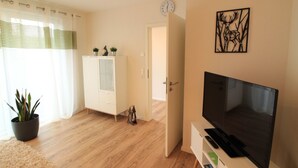 Ein modernes Wohnzimmer mit Flachbildfernseher, einem weißen Schrank mit Glastüren, einer Topfpflanze und einem Wandbild.