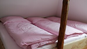 En enkeltseng med sengegavl i træ og et sengetæppe med rosa striber.