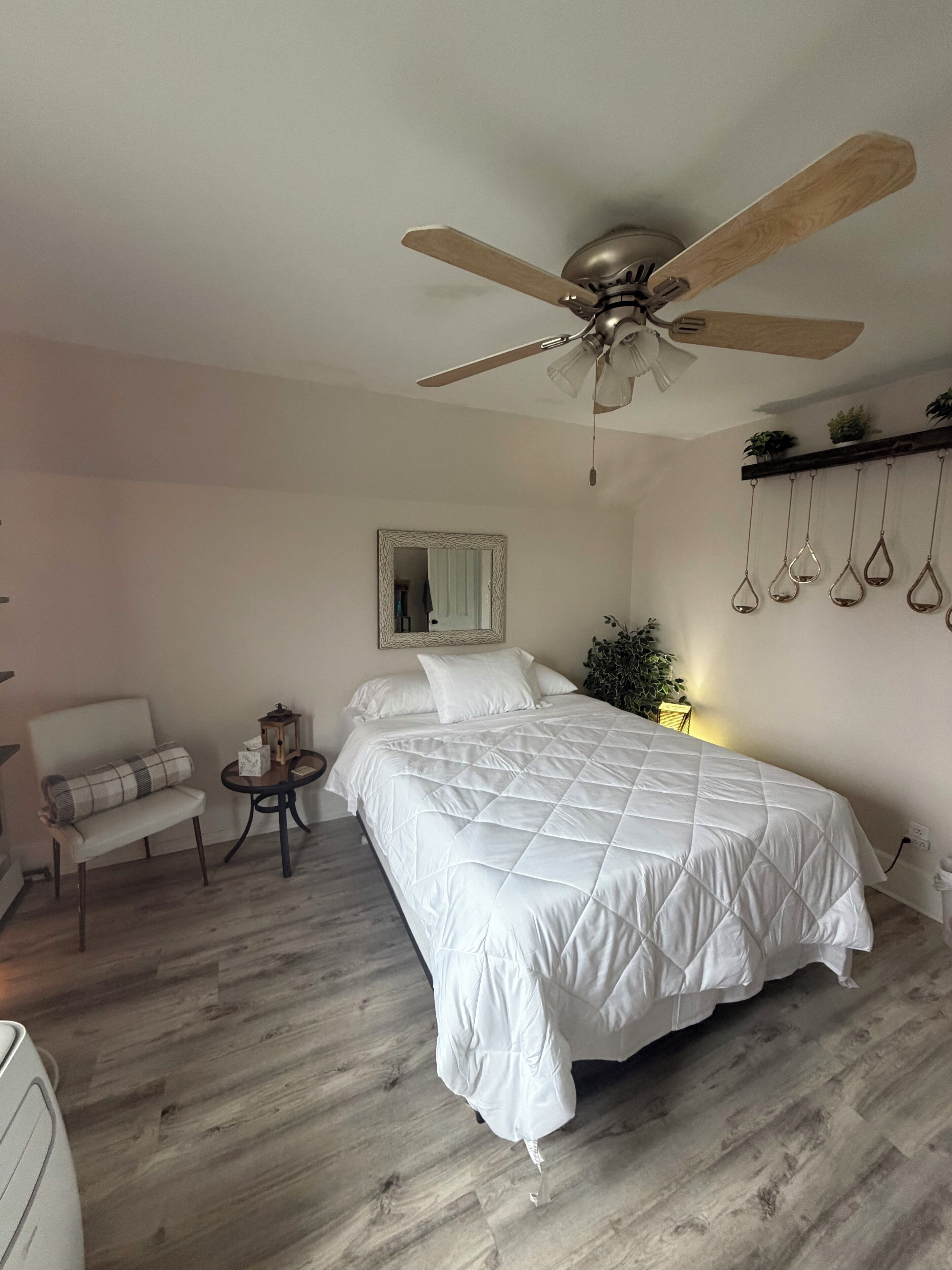 Une chambre à coucher avec un grand lit, un ventilateur de plafond, une table de chevet, une chaise et un miroir.