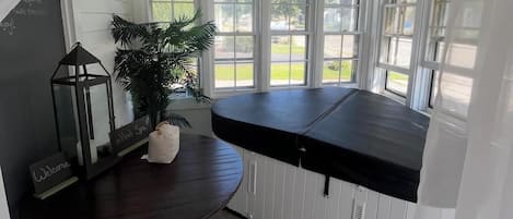 A cozy corner with a dark wooden table, a white cushioned bench, a potted plant, and a "Welcome" sign.