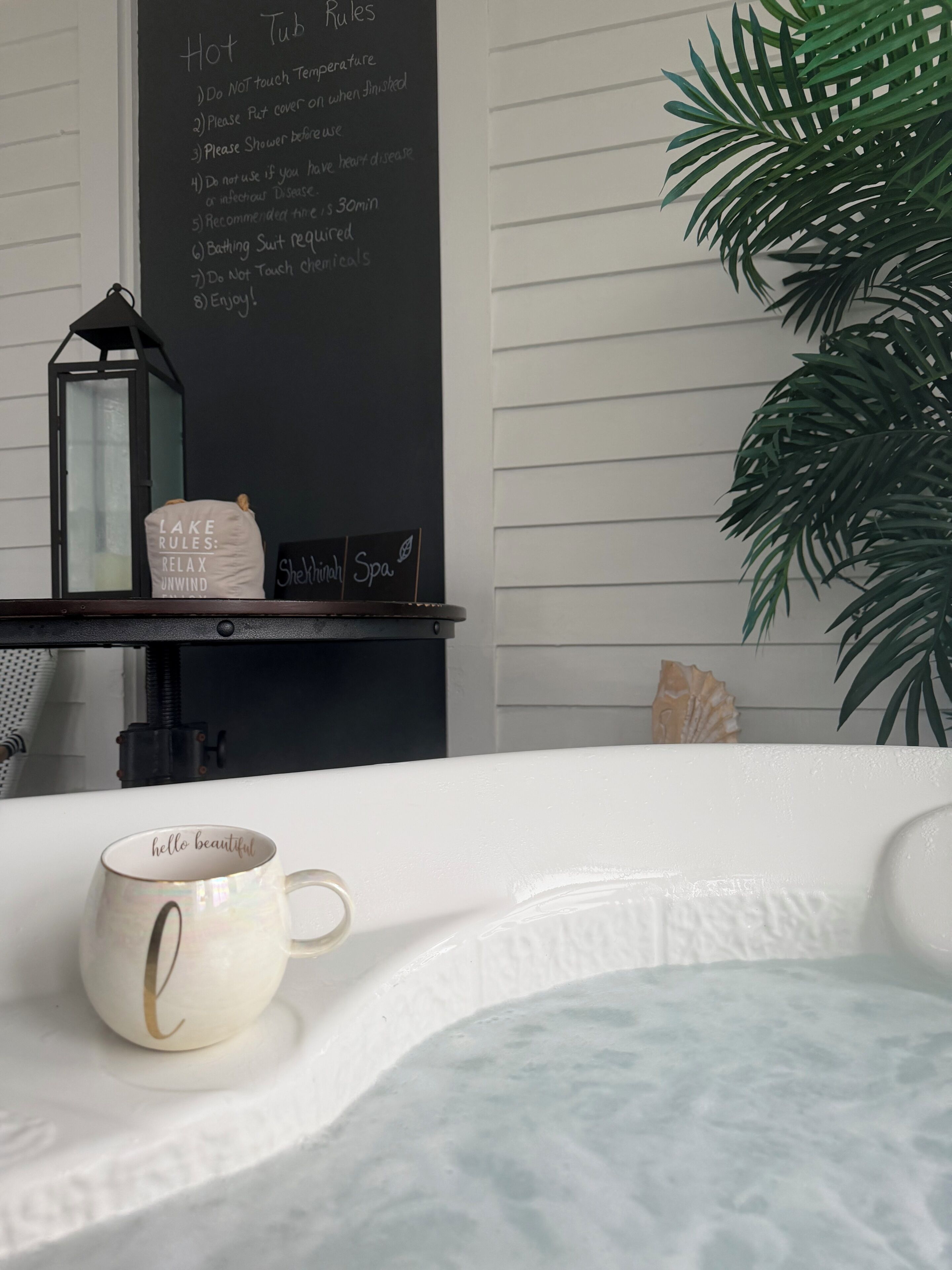 A spa area with a hot tub, a chalkboard with rules, a decorative lantern, and a plant.