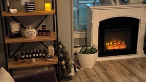 En hyggelig stue med pejs, en reol med diverse genstande, og et lille juletræ.
