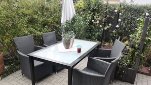 Une terrasse extérieure avec une table à plateau de verre et des chaises en osier.