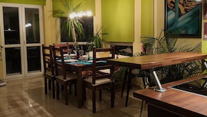 Un coin repas avec une table dressée pour quatre personnes, entourée de chaises, d’un mur vert et d’un tableau.