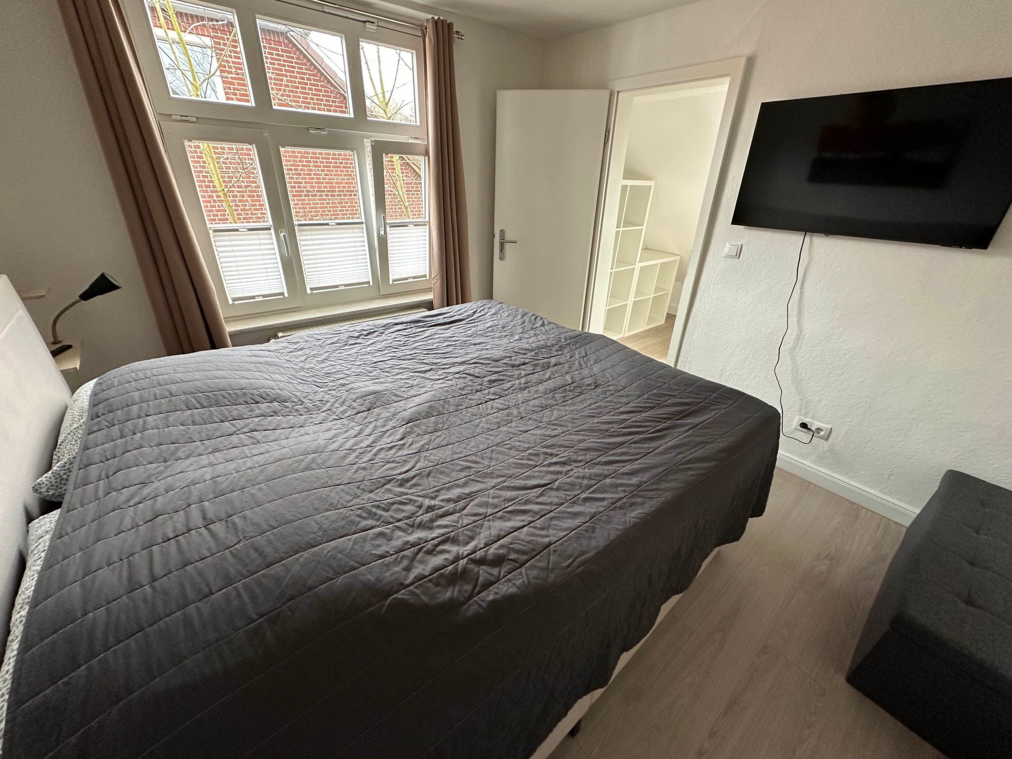 A bedroom with a large bed, a TV mounted on the wall, and a window with curtains.