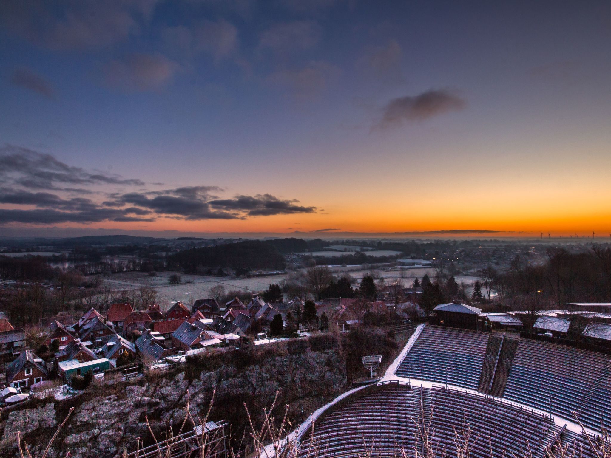A panoramic view of a town at sunset with a large stadium in the foreground.