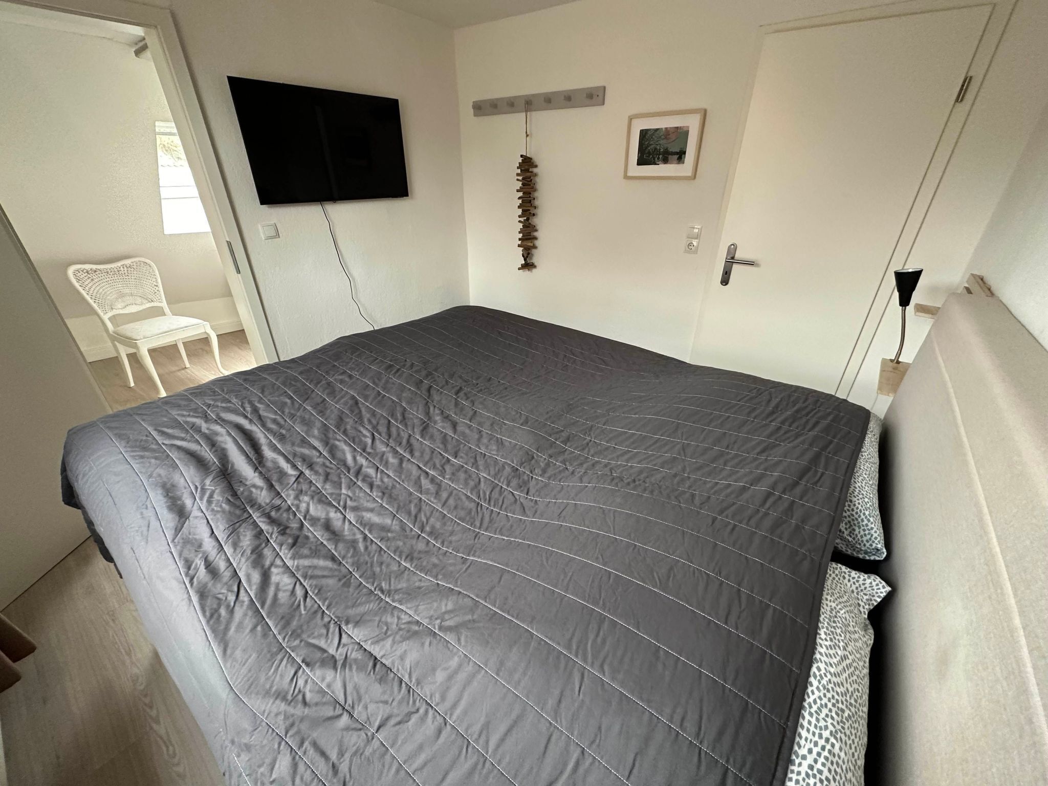 Ein Schlafzimmer mit einem großen Bett, einem an der Wand befestigten Fernseher, einem Sessel und einer Tür.