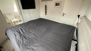 Ein Schlafzimmer mit einem großen Bett, einem an der Wand befestigten Fernseher, einem Sessel und einer Tür.