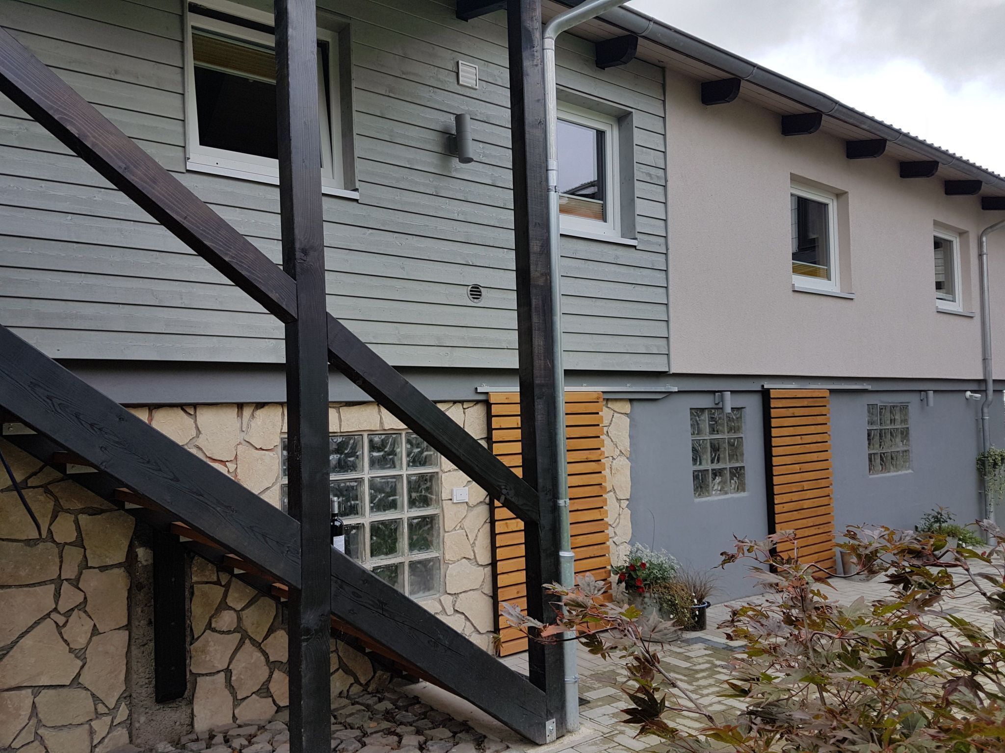 A two-story house with a stone foundation, wooden shutters, and a visible staircase.
