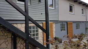 Une maison à deux étages, avec des fondations en pierre, des volets en bois et un escalier apparent.