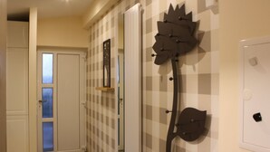 Un couloir avec un motif à carreaux sur le mur, une porte dotée de panneaux en verre dépoli et un élément décoratif en métal fixé au mur, ressemblant à une fleur.