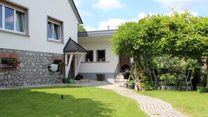 Een huis met een stenen muur, een kleine tuin, een barbecueplek en een verhard pad.