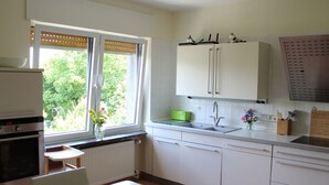 Een keuken met witte kasten, een houten tafel, een raam met zonwering en een radiator.