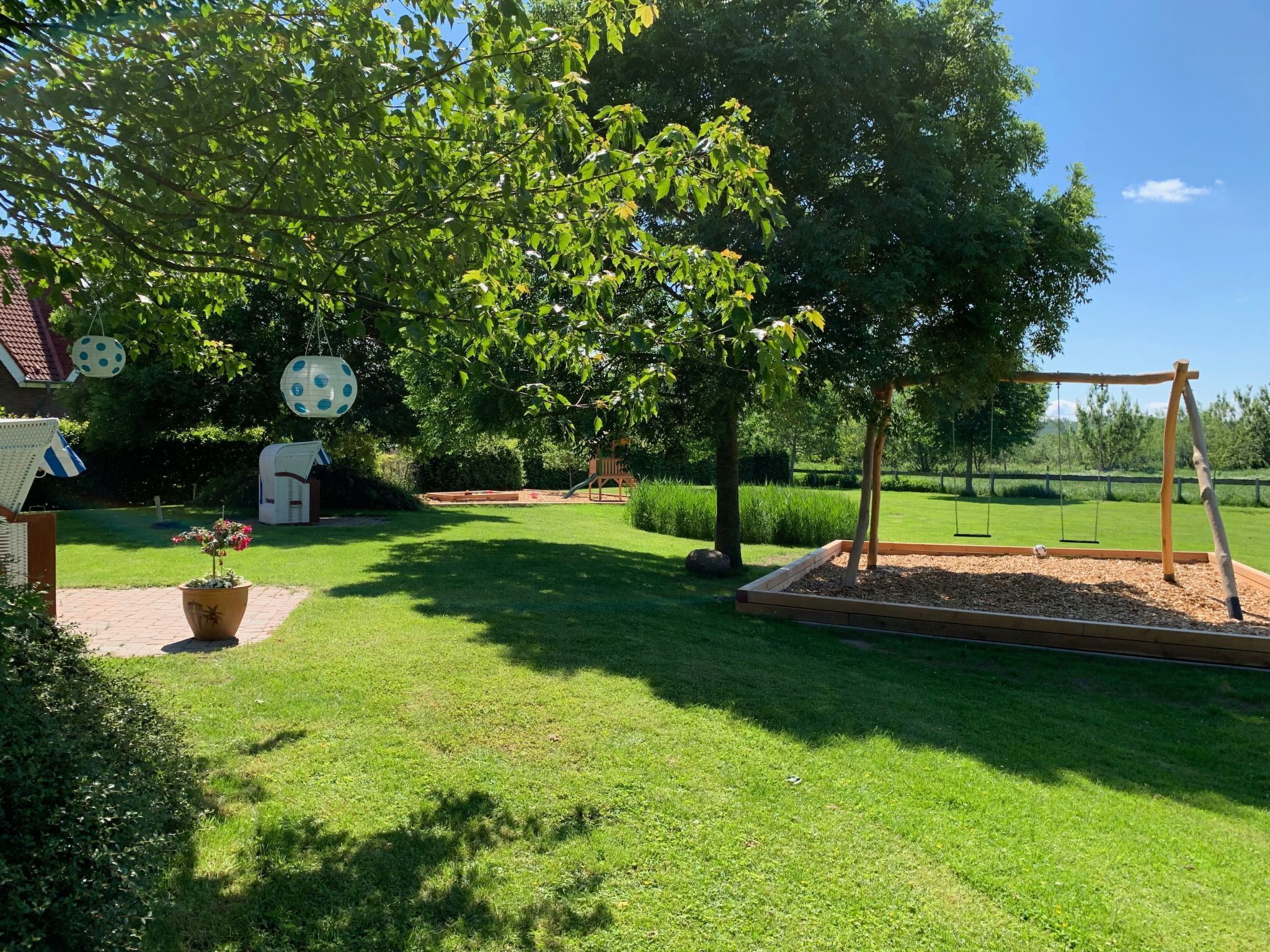 A well-maintained garden with a swing set, a playhouse, and a large tree providing shade.